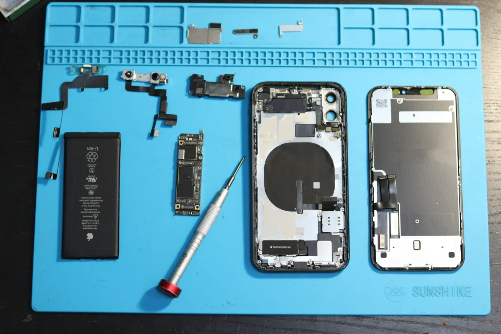 Composants d’un iPhone démontés sur un tapis de réparation : batterie, carte, caméras et châssis